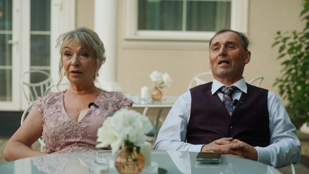 Dwoje gości przy stoliku opowiada podczas wywiadu do dokumentalnego filmu ślubnego, mikroporty przy ubraniu
